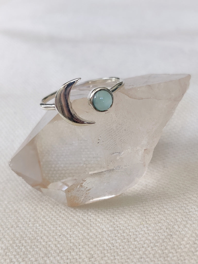 This is a sterling silver ring with a crescent moon and chalcedony stone that is light blue in colour, sitting on top of a clear quartz crystal, that are both from our third eye crystal and jewellery store in Auckland New Zealand