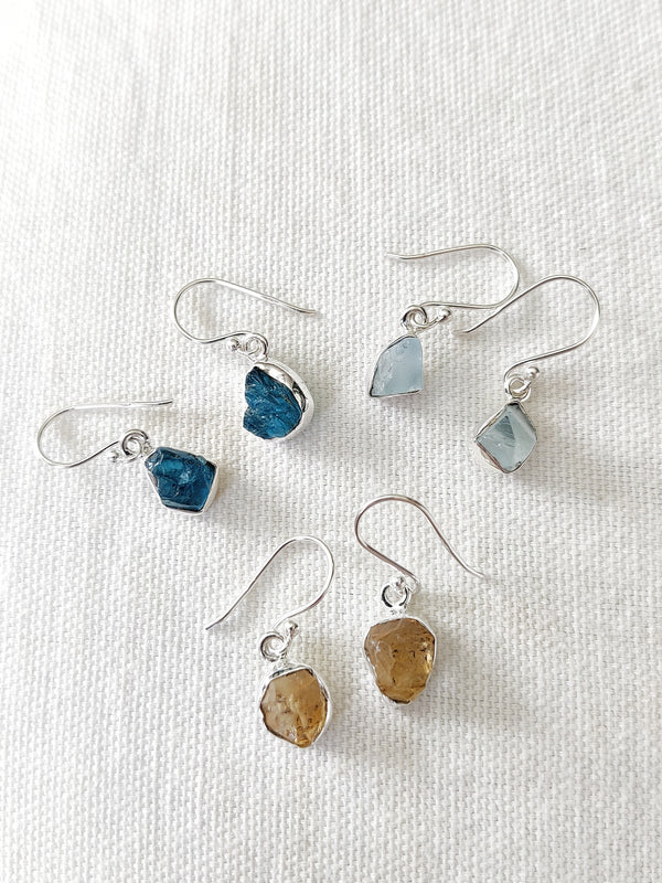 This is three pairs of rough cut sterling silver earrings, one pair is made with apatite crystals, dark blue in colour, one pair is made with aquamarine crystals that are light blue in colour and one pair is made with citrine crystals, all of which are available at our third eye crystal and jewellery store in Auckland, New Zealand