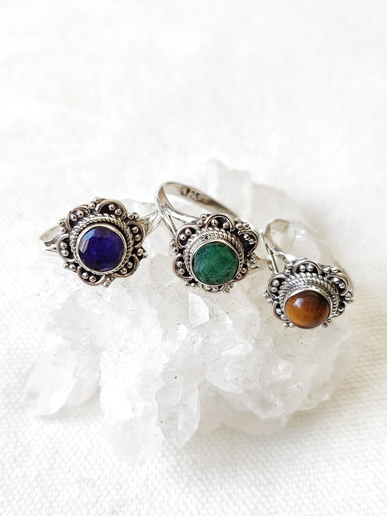 This is three sterling silver rings with a floral design and and a crystal gemstone. One has a sapphire gemstone dark blue in colour, one has an emerald gemstone dark green in colour and one has a tigers eye gemstone brown in colour, all available from our third eye crystal and jewellery store in Auckland New Zealand