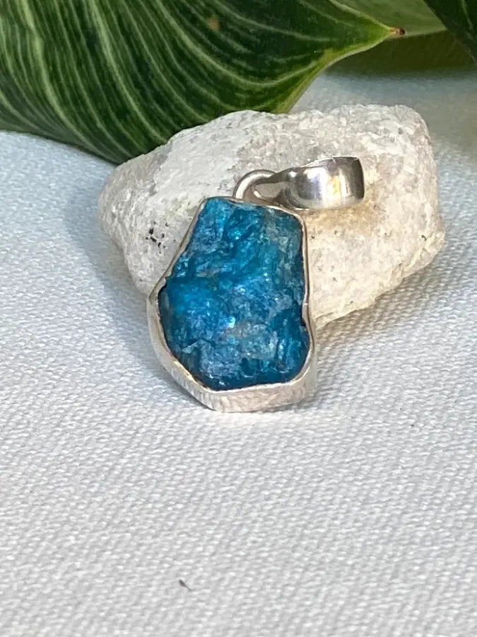 Blue Apatite stone pendant on a silver chain against a textured white background