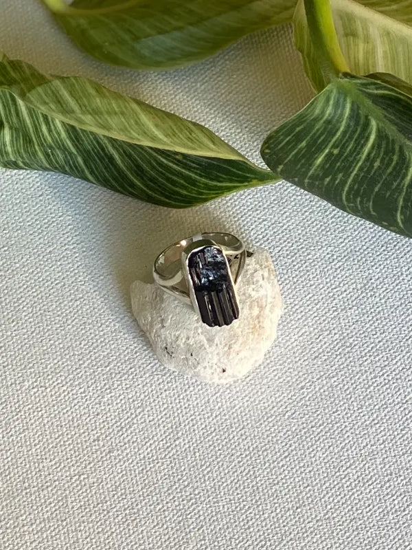 Silver ring with a black rough tourmaline gemstone on a textured surface with green leaves