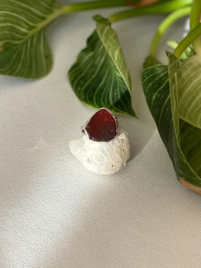  Large red rough garnet stone ring on a light surface with green leaves in the background
