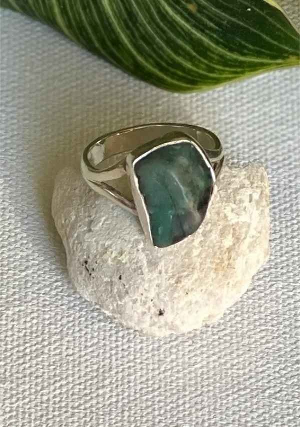 Silver ring with a green emerld stone on a textured surface with a leaf in the background