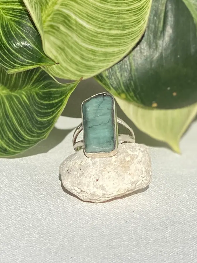 Ring with a green rough emerald stone on a rock with green leaves in the background