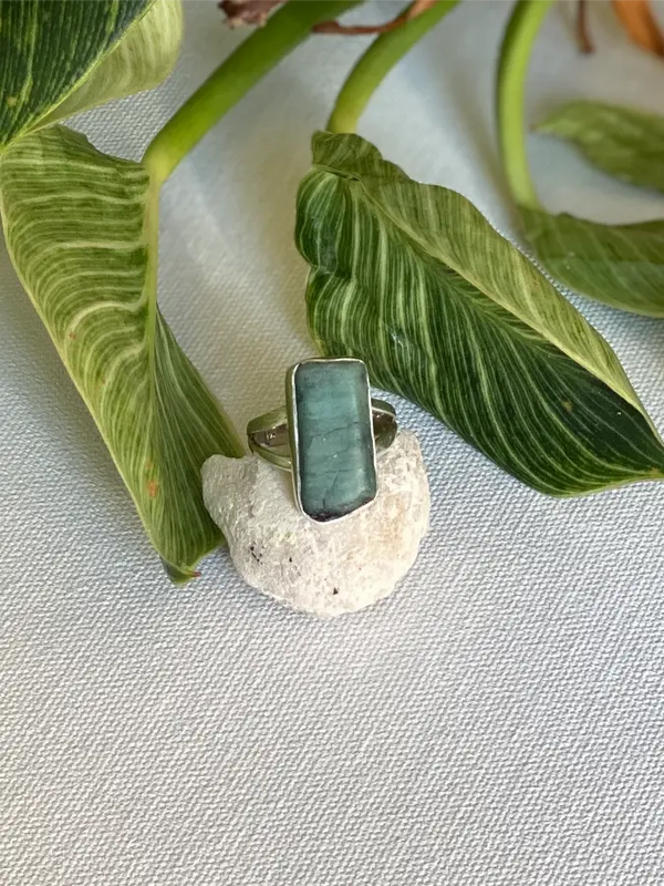 Silver ring with a green rough emerald stone on a textured surface with leaves in the background