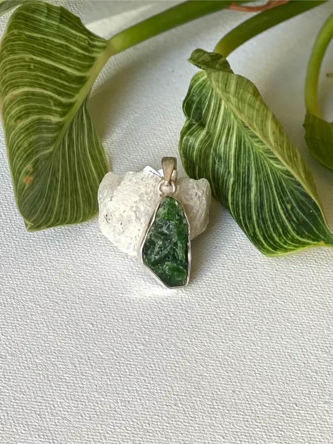 Green Dioptase stone pendant set in a sterling silver bezel. White stone with green leaves in the background
