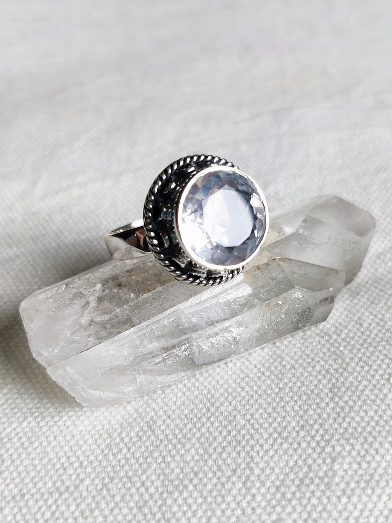 This is a sterling silver bezel set and detailed rose quartz ring, light pink in colour, sitting on top of a clear quartz crystal, both available at our third eye crystal and jewellery store in Auckland, New Zealand