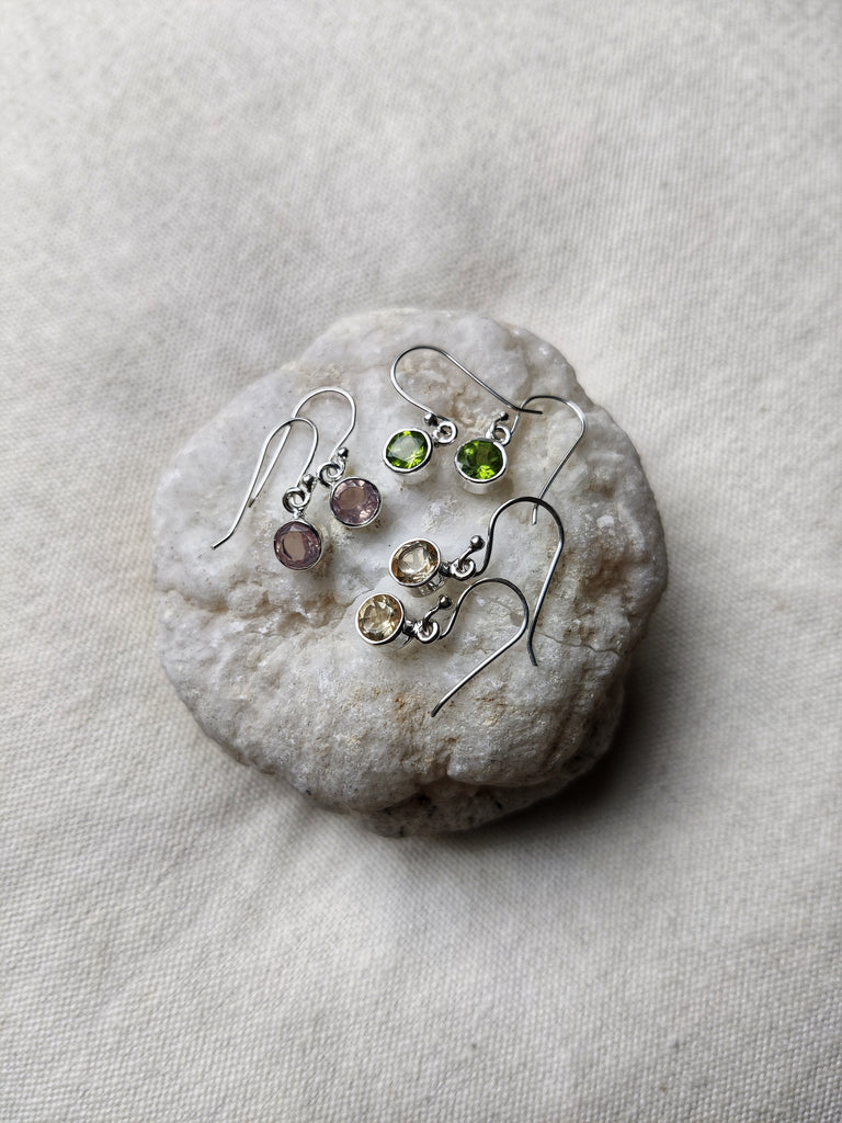 This is three sets of sterling silver circle gemstone earrings sitting on a crystal. One set of earrings are amethyst, light purple in colour, another is peridot, light green in colour and the final pair are citrine, yellow in colour. All are available at our third eye crystal and jewellery store in Auckland, New Zealand. 