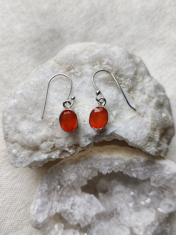 This is a pair of sterling silver oval shaped earrings with a carnelian gemstone that is orange in colour, sitting on stop of a crystal, both available at our third eye crystal and jewellery store in Auckland, New Zealand
