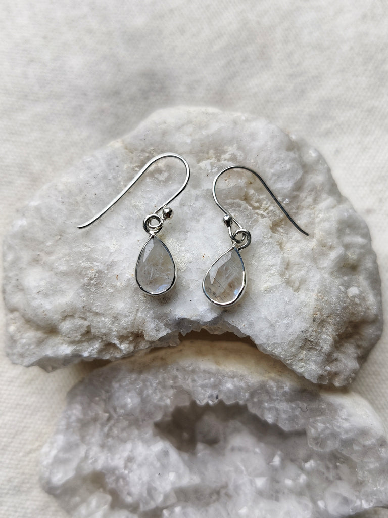 This is three pairs of sterling silver crystal teardrop shaped earrings sitting on top of a crystal, one set of earrings have a rose quartz crystal that is light pink in colour, one pair has an onyx crystal that is black in colour and one pair has a moonstone crystal that is rainbow white in colour, all are available at our third eye crystal and jewellery store in Auckland, New Zealand