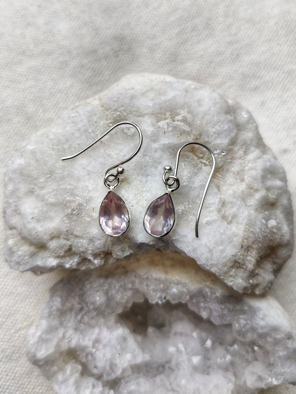 This is a pair of sterling silver teardrop shaped earrings with a rose quartz crystal gemstone that is pink in colour, sitting on top of a crystal, all available at our third eye crystal and jewellery store
