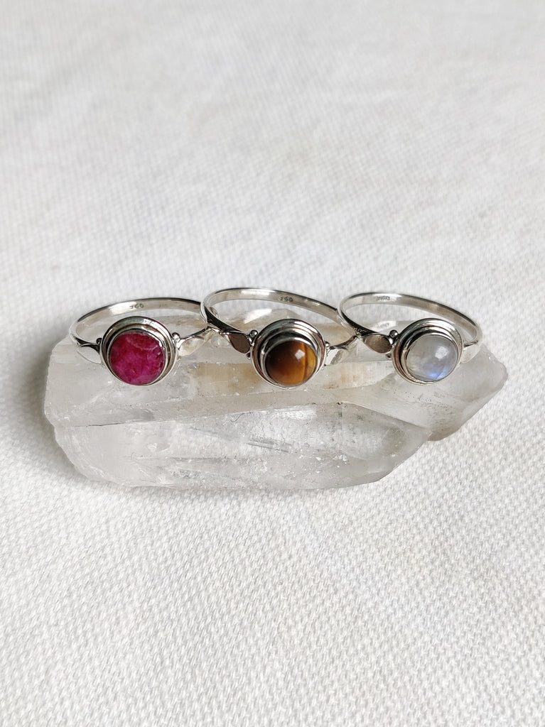 This is three sterling silver rings with a simple design and a crystal gemstone. One ring has a ruby crystal that is hot pink in colour, one has a tigers eye crystal that is brown in colour and one is a moonstone crystal that is rainbow white in colour, all available at our third eye crystal and jewellery store in Auckland, New Zealand.