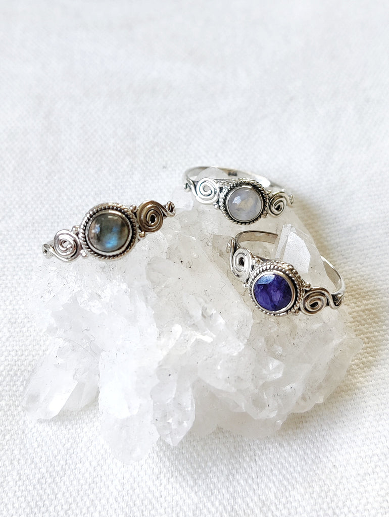 This is three sterling silver rings with a spiral design and a crystal gemstone. One ring has a labradorite  crystal that is rainbow grey in colour, one has a moonstone crystal that is rainbow white in colour and one is a sapphire crystal that is dark blue in colour, all available at our third eye crystal and jewellery store in Auckland, New Zealand.